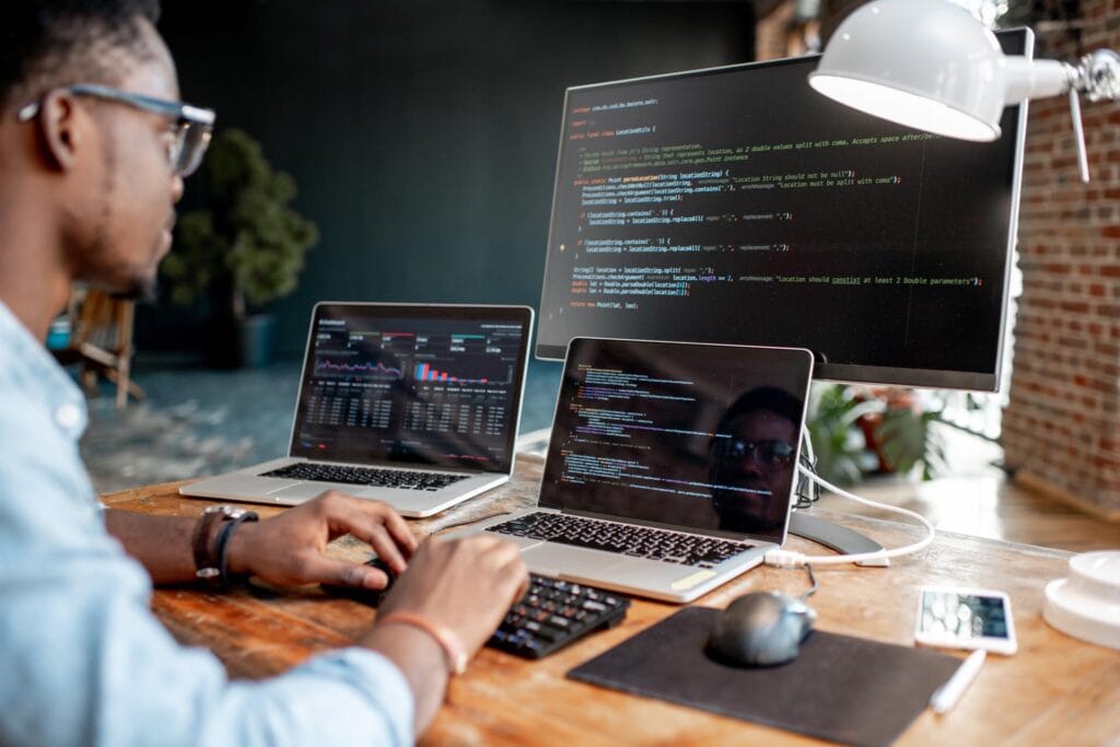 man writing lines of code on three screens