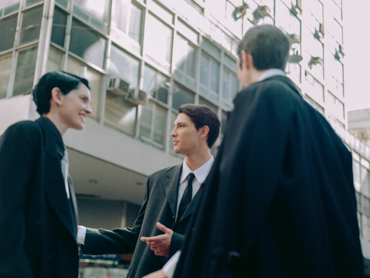 Three people standing outside building all wearing black suits talking to eachother