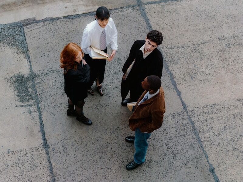Group of work colleagues standing around outside talking to each other holding folders